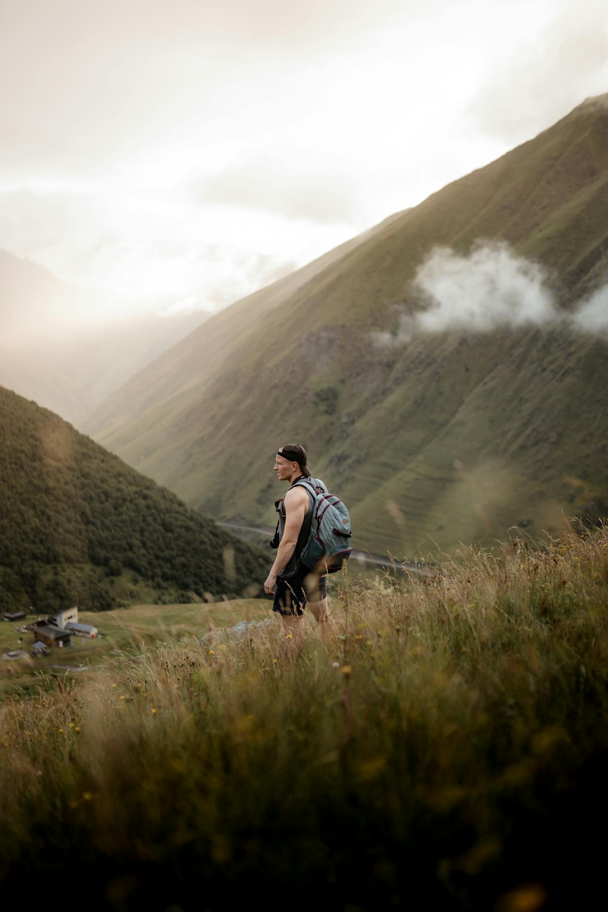 Man wearing a travel backpack while hiking through a green mountain valley at golden hour