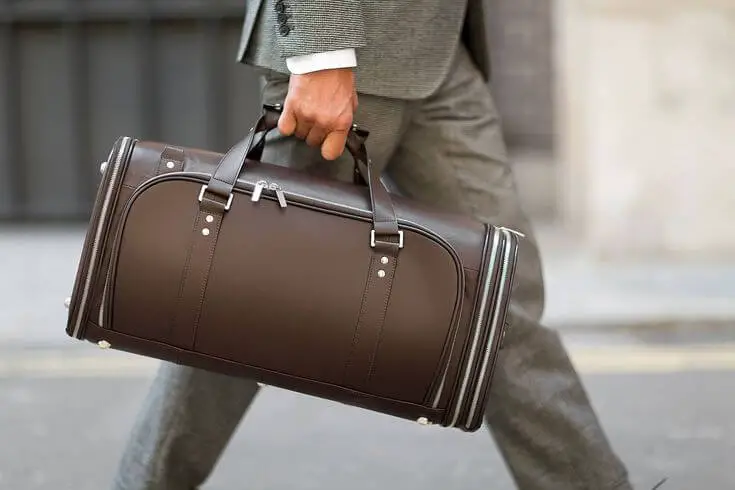 man in business suit walking with leather, luxury garment bag