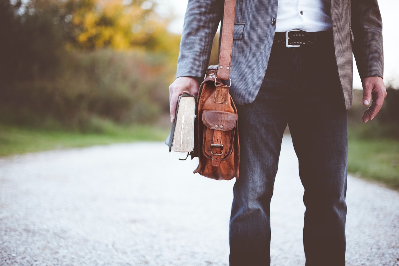 Man holding book and used leather shoulder luggage