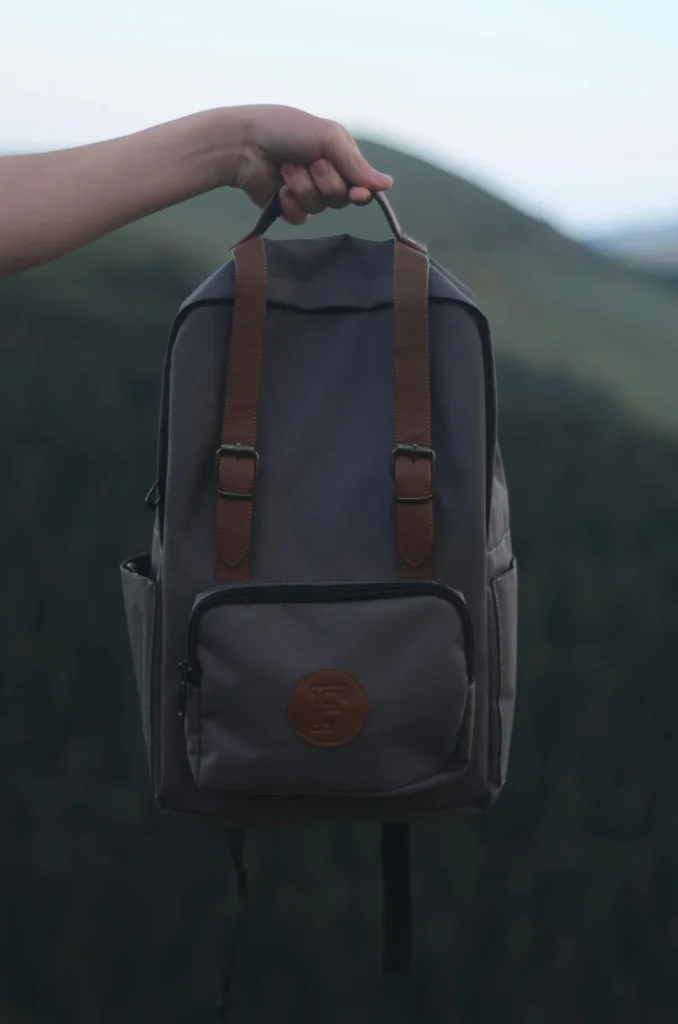 Gray backpack with brown leather straps held up against a mountain backdrop