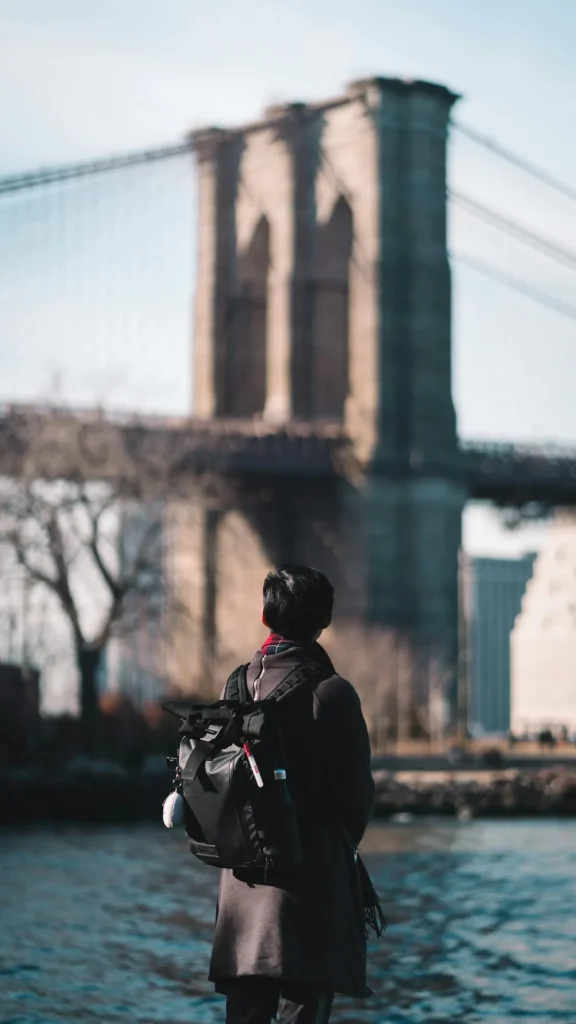Traveler wearing a backpack while exploring a city with a bridge in the background