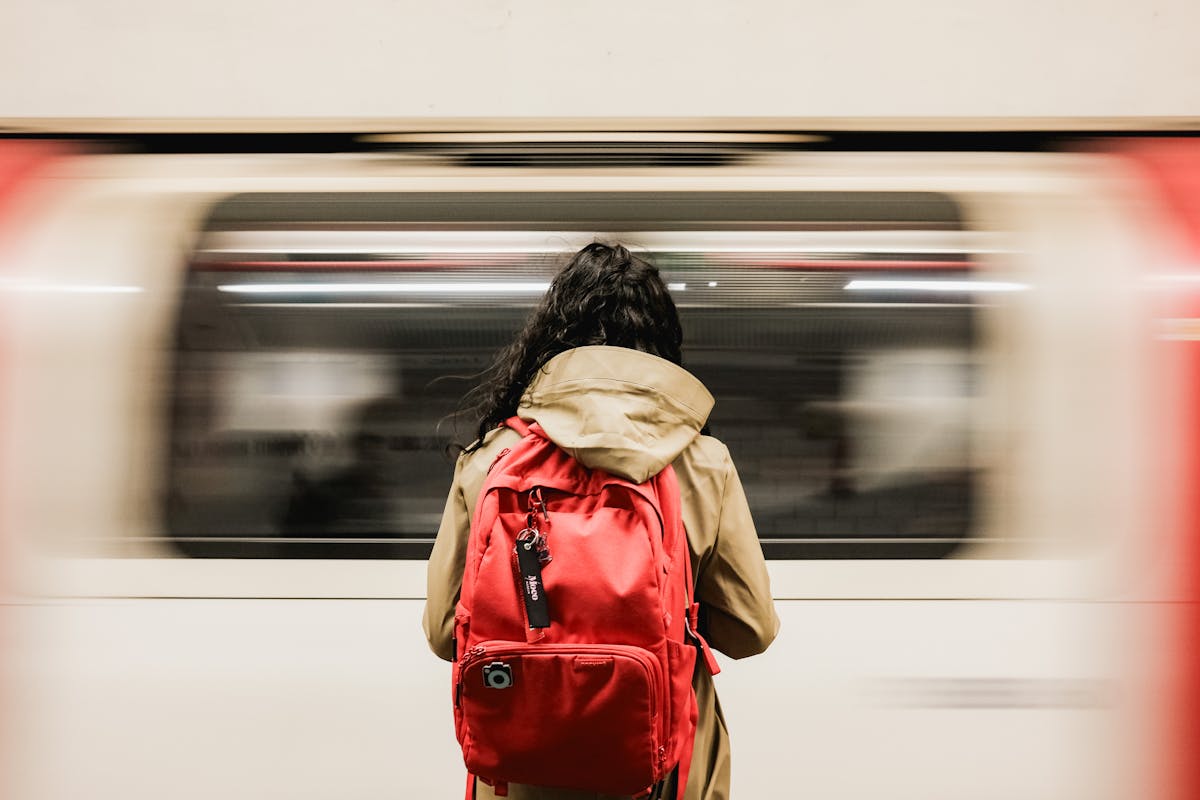 Commuter wearing a backpack waiting at a subway platform as a train passes