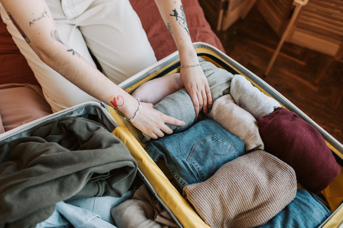 Close-up of hands packing various clothing items into a suitcase for travel