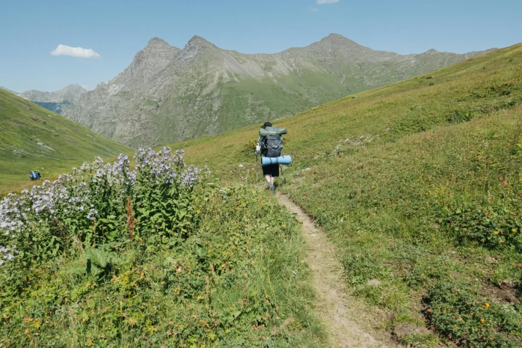 Hiker walking a narrow mountain trail with a fully loaded backpack and trekking poles