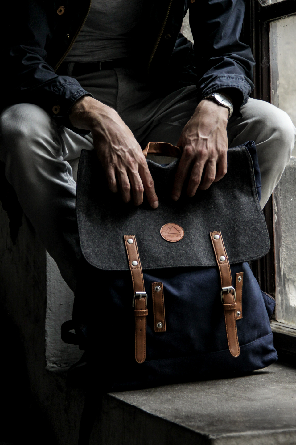 Man sitting in an urban setting holding a compact canvas and leather mini backpack