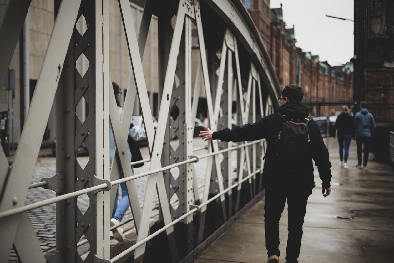 Man walking along an urban bridge with a travel backpack on a cloudy day