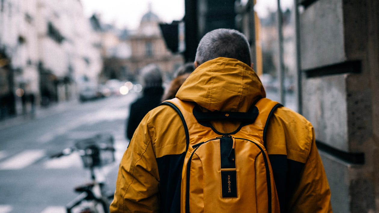Man wearing a yellow jacket and sling backpack walking down a city street