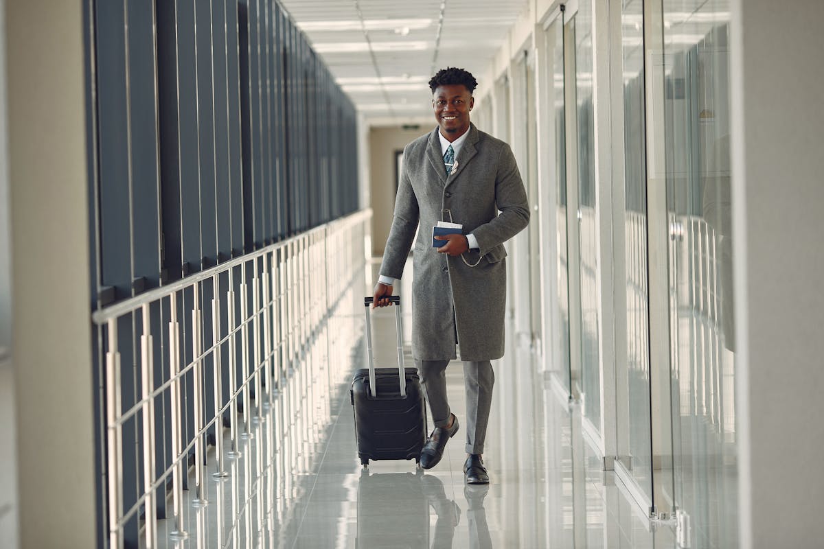 Traveler walking through a bright airport corridor while pulling a hardside carry-on suitcase and holding a passport