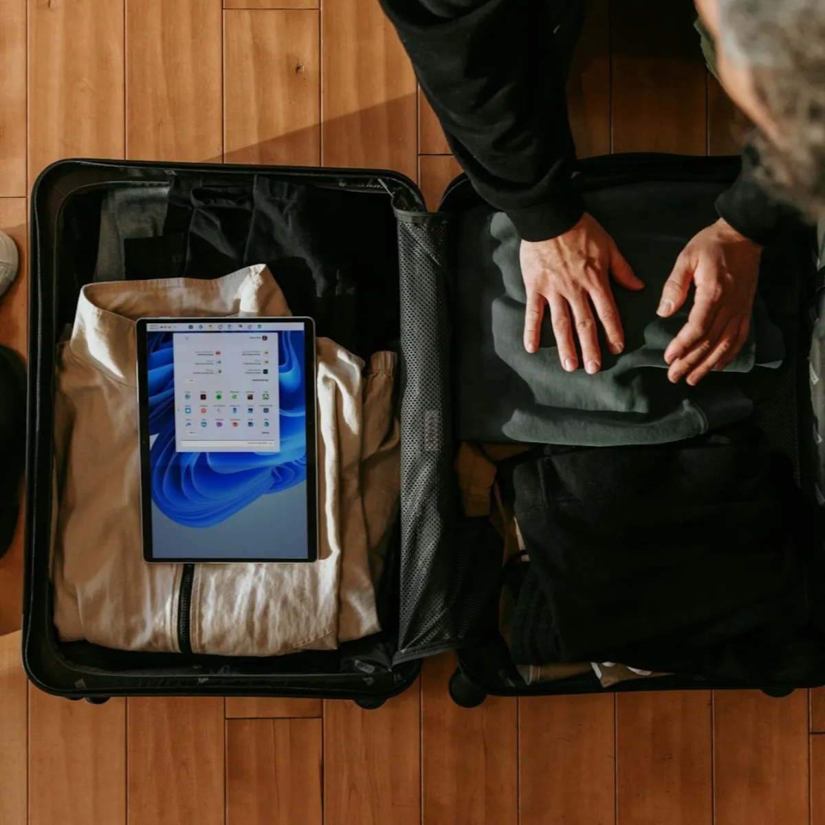 Overhead view of a traveler packing an open carry-on with folded clothes, tablet, and shoes, planning the trip strategically.