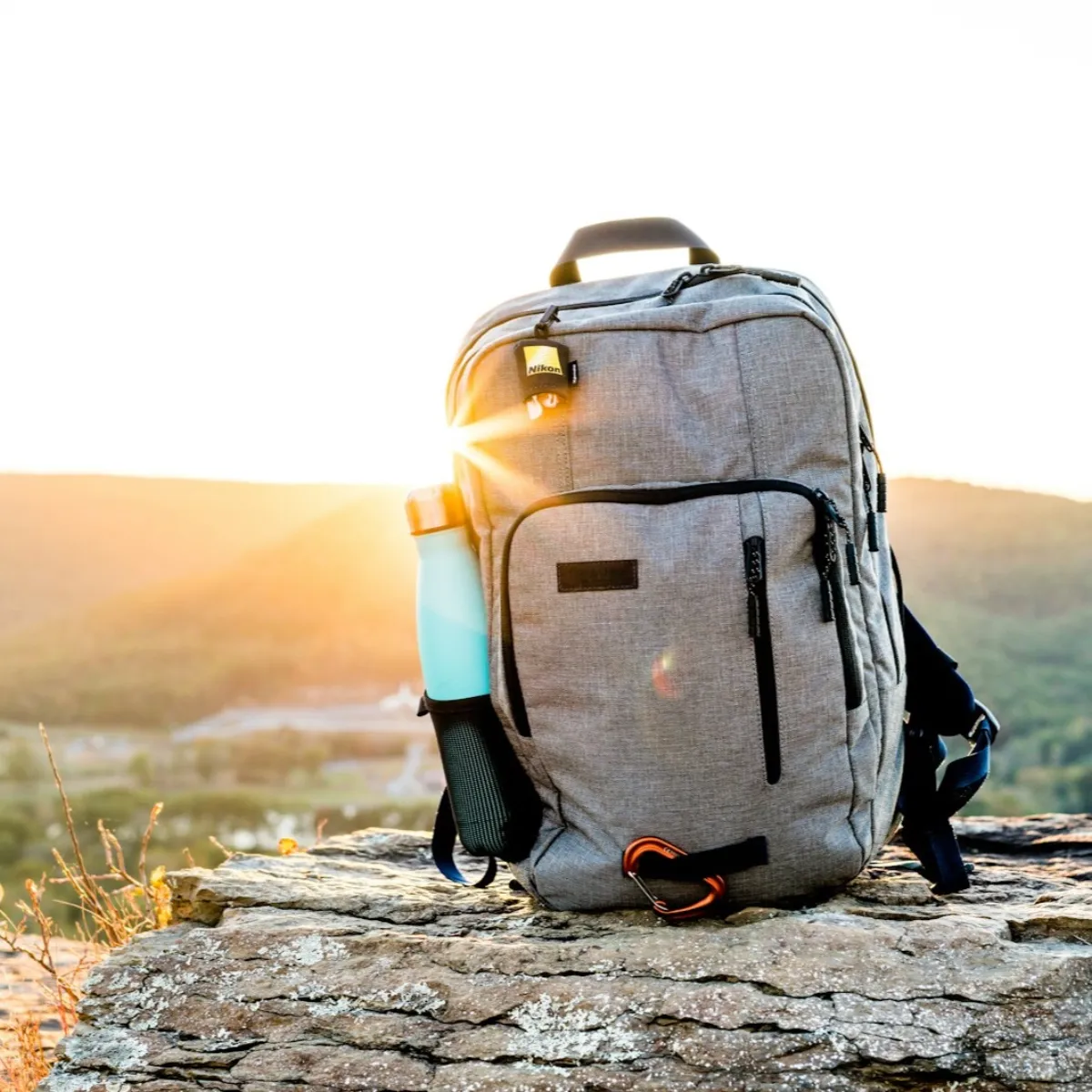 Lightweight grey ultralight-style backpack with a water bottle resting on a rock at sunset, showing minimalist gear design.