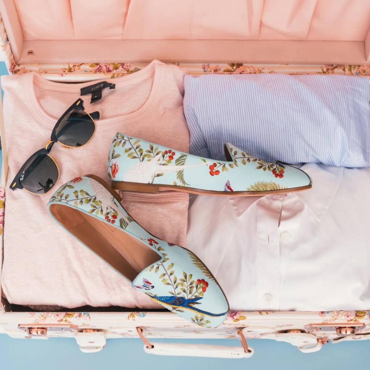 Open suitcase flat-lay packed with neatly folded shirts, shoes, and sunglasses showing organized space-saving packing.