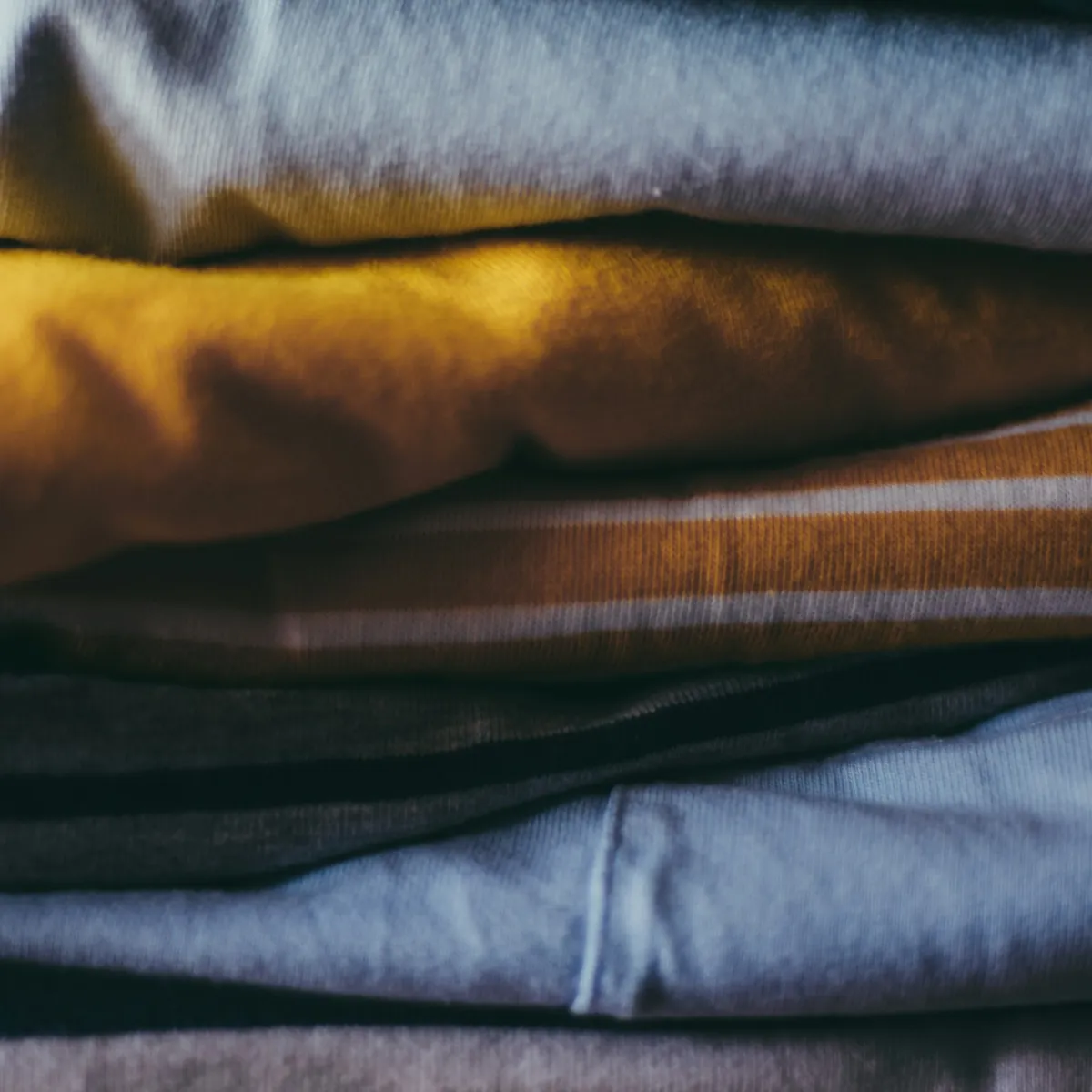 Neatly stacked folded shirts in earth tones showing the tight, compact look of ranger-rolled garments.