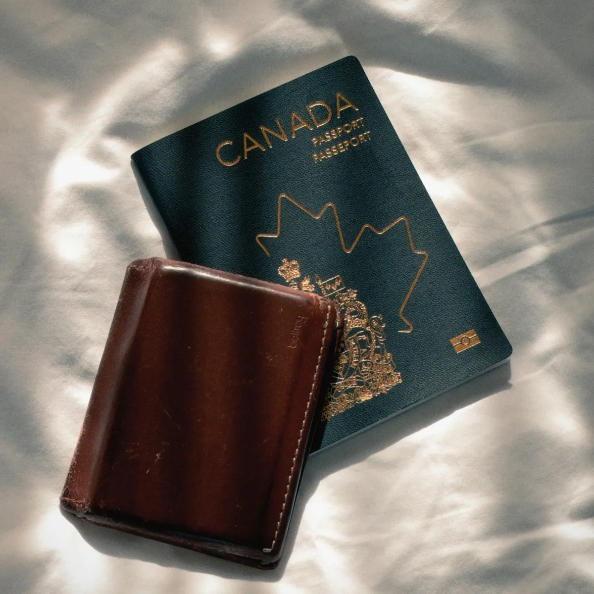 Passport next to a brown leather travel wallet on a light fabric background, organized for a trip.