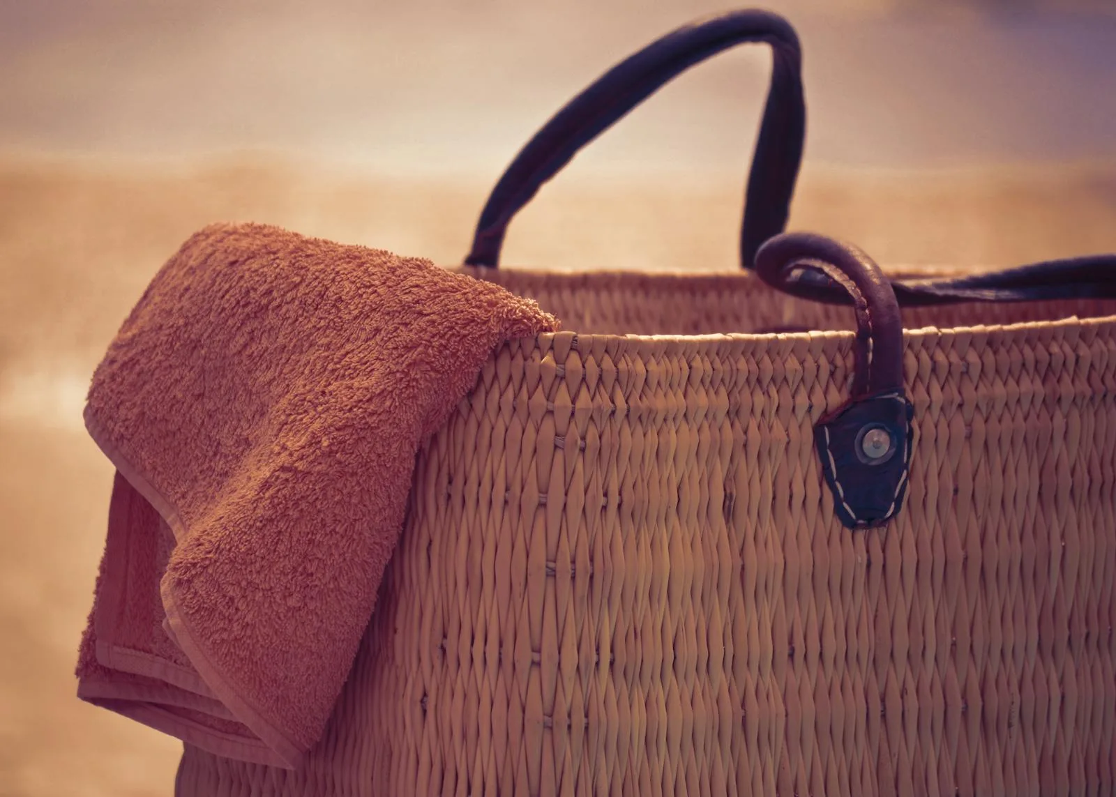 A straw beach bag with a towel draped over it, perfect for a summer day at the shore.