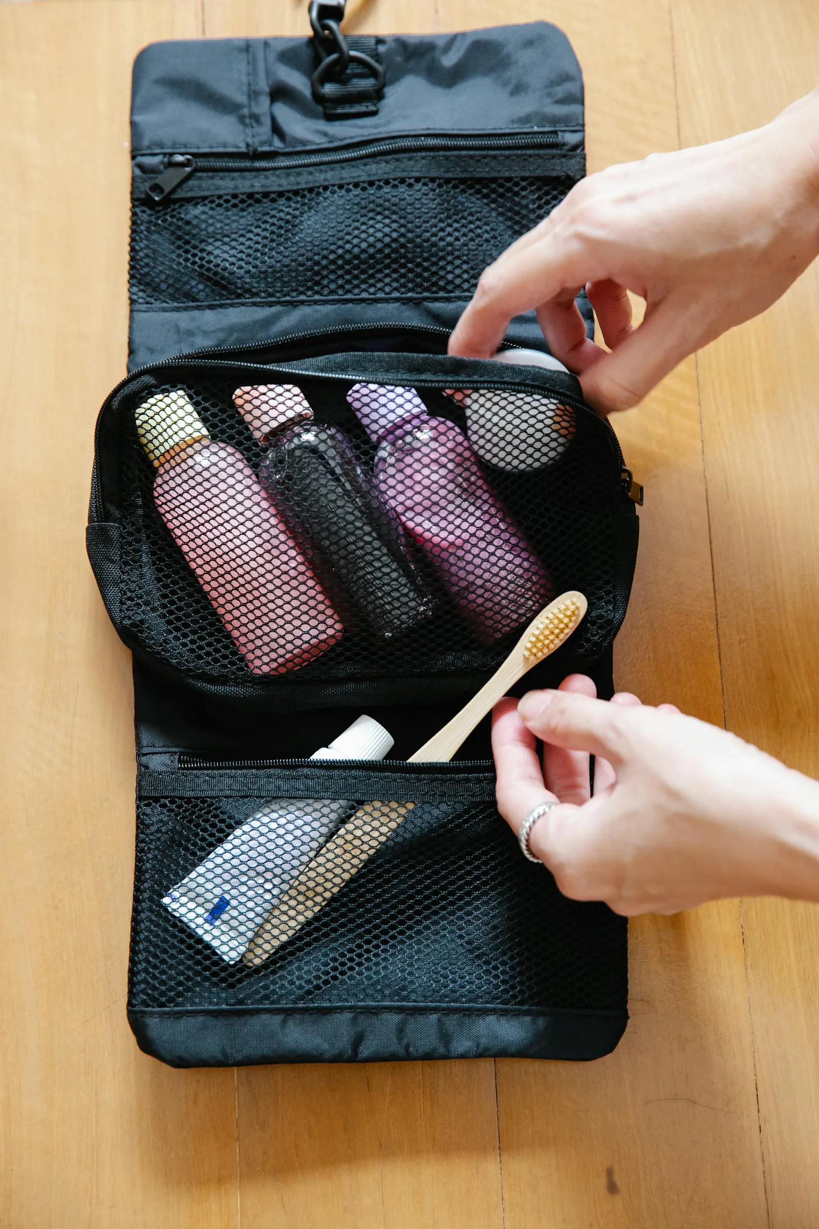 Open toiletry bag with bottles and a bamboo toothbrush on a wooden surface