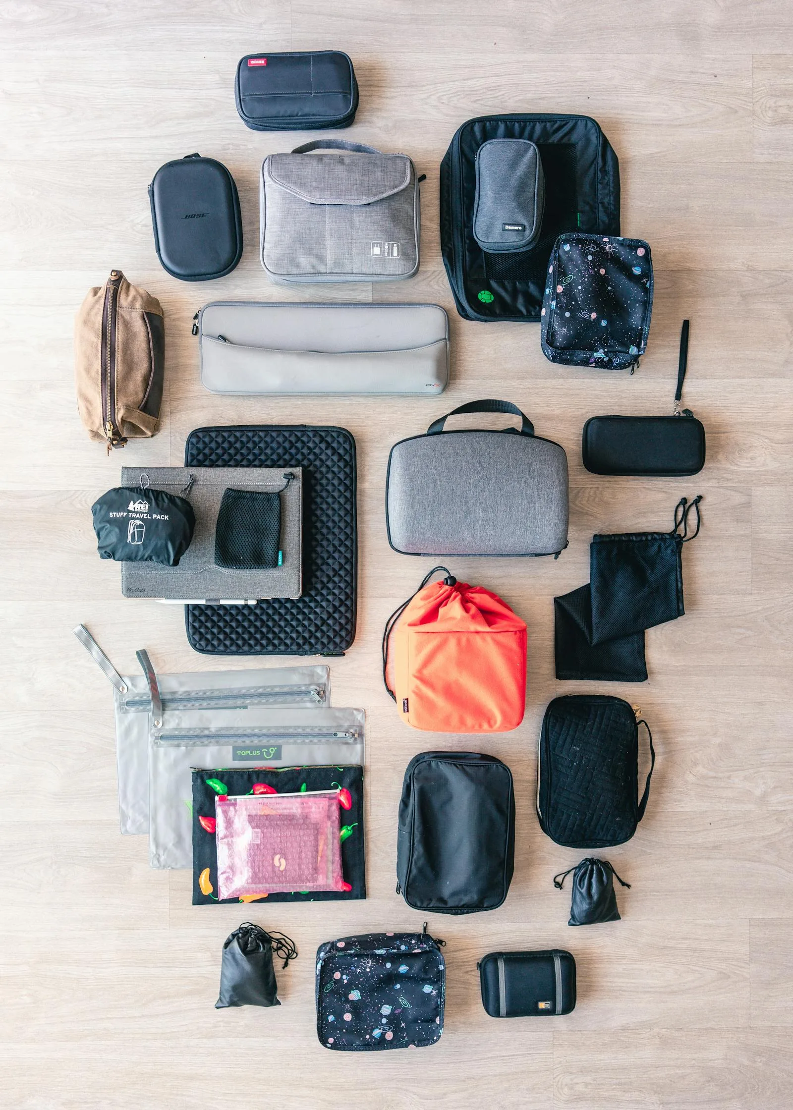 Flat lay of assorted travel bags and accessory pouches on a wooden floor