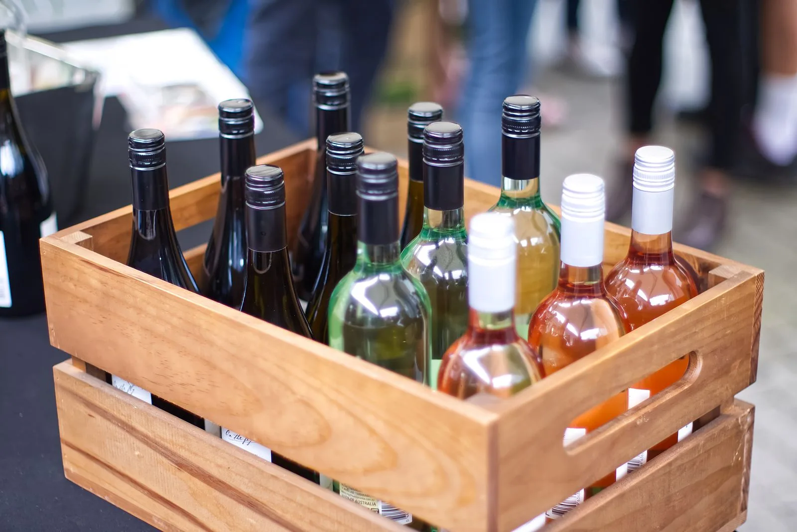 A wooden crate filled with diverse wine bottles at an outdoor gathering