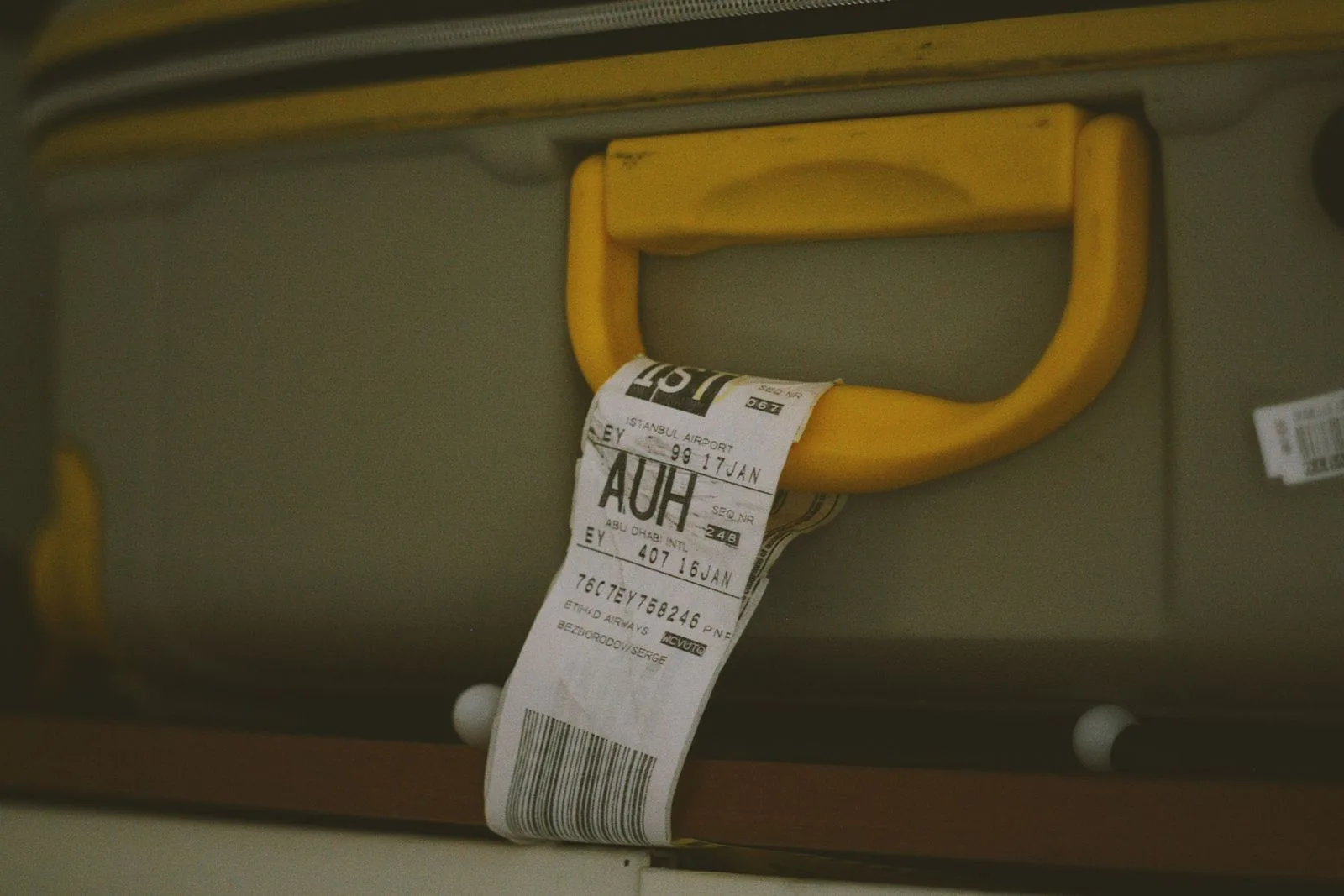 Close-up of a yellow suitcase handle with a visible travel tag and barcode, ideal for travel themes