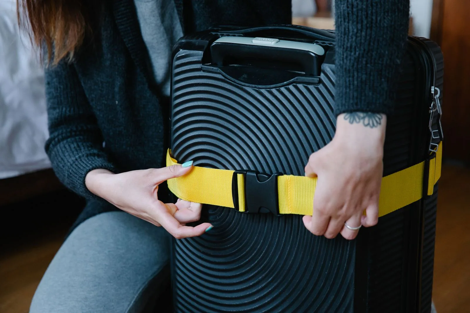 Close-up of hands fastening a bright yellow strap around a black suitcase