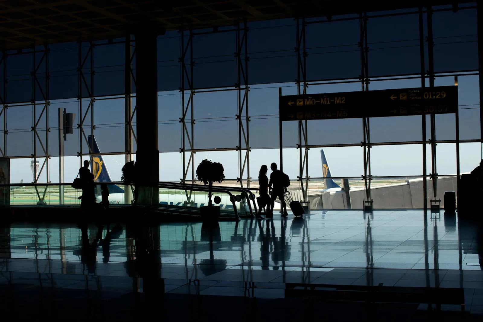 Travelers silhouetted in a modern airport terminal with glass windows and visible airplane tails