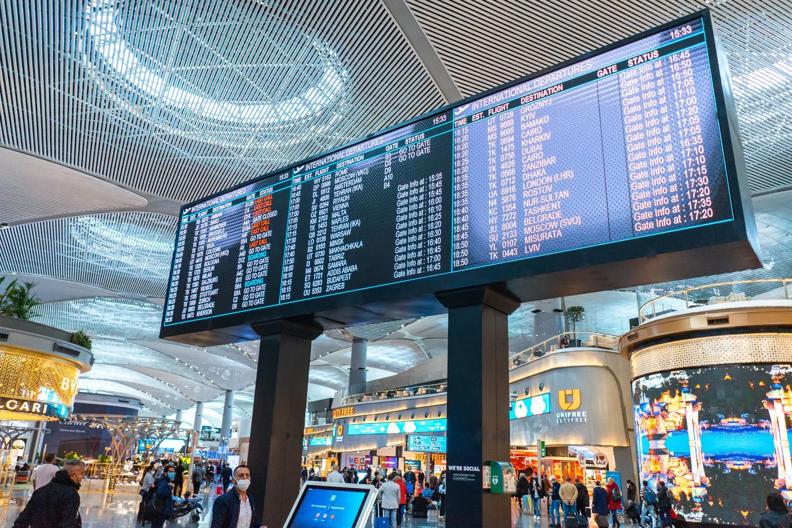 Passengers walk through Istanbul Airport's departure area, surrounded by stores and flight information displays