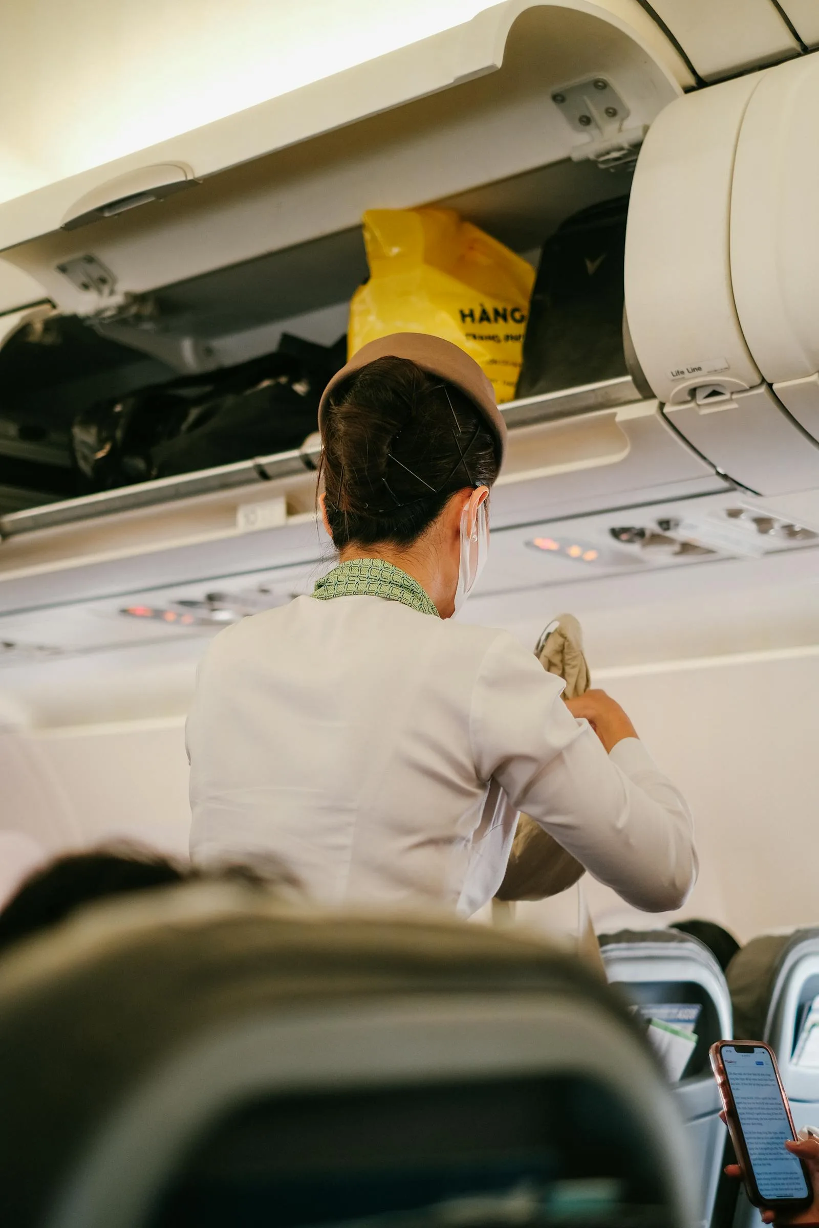 A flight attendant assists passengers with luggage in an airplane cabin