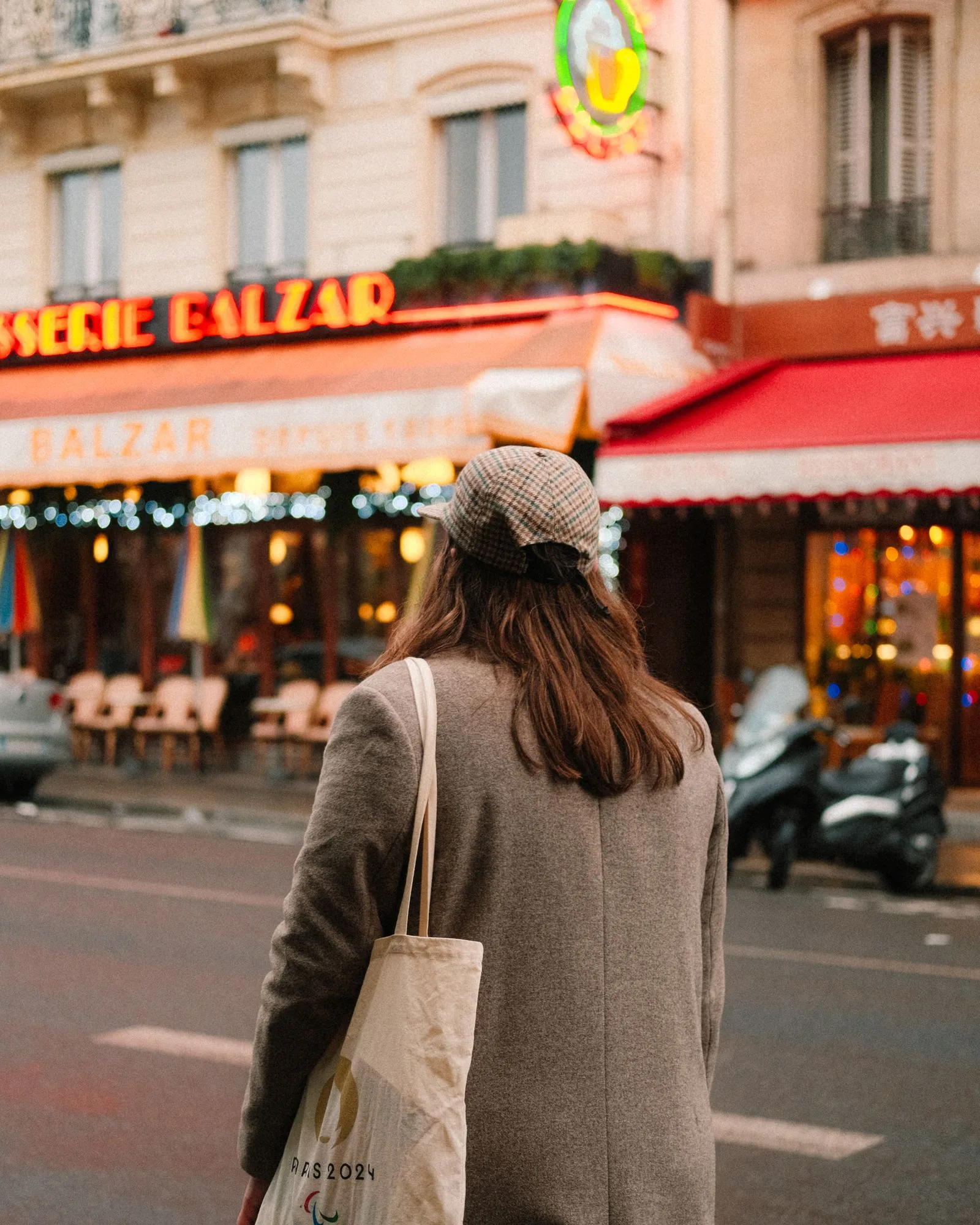A woman with a tote stands before a Parisian café, capturing urban charm.