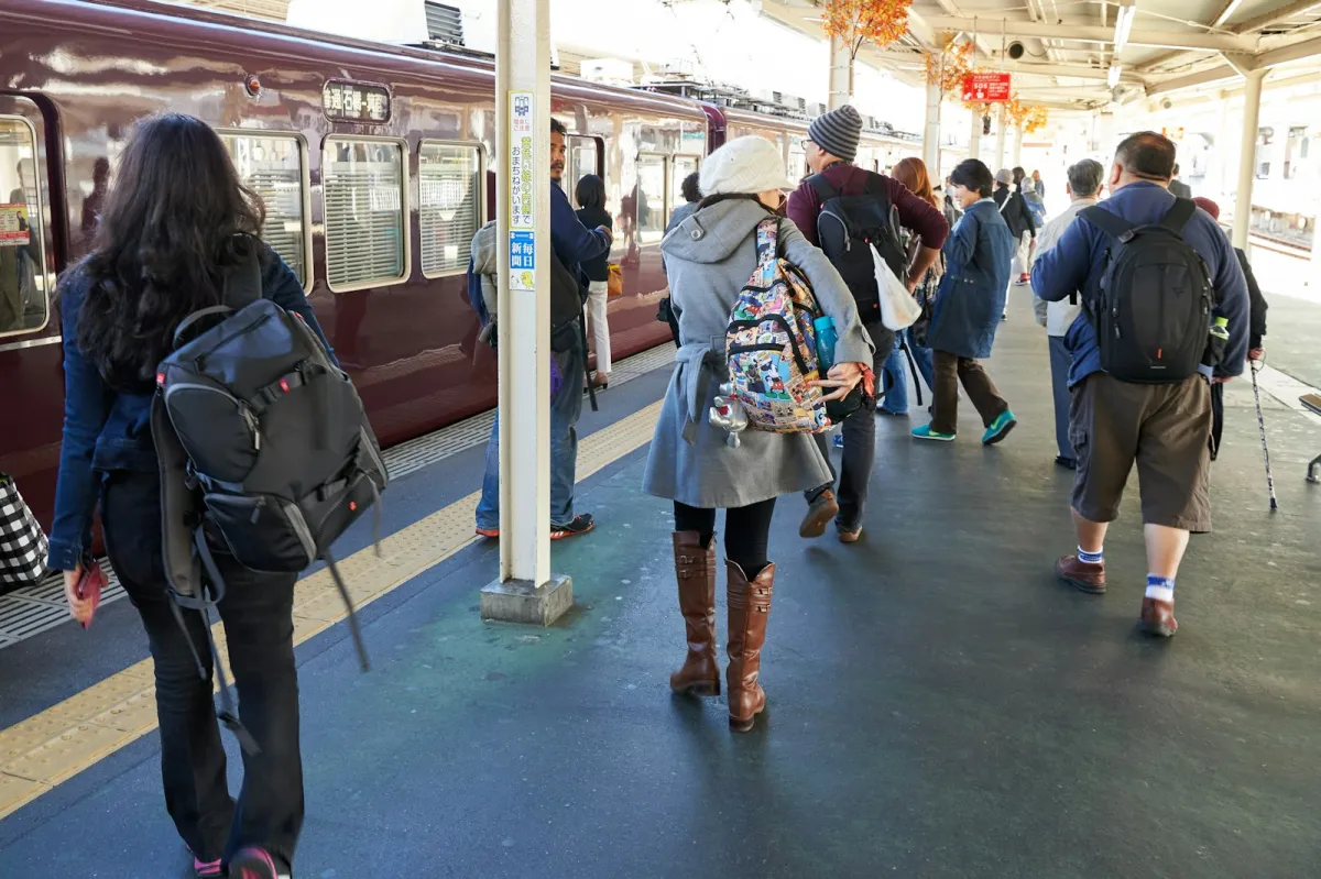 Commuters carrying backpacks and bags along a busy train platform beside a waiting train