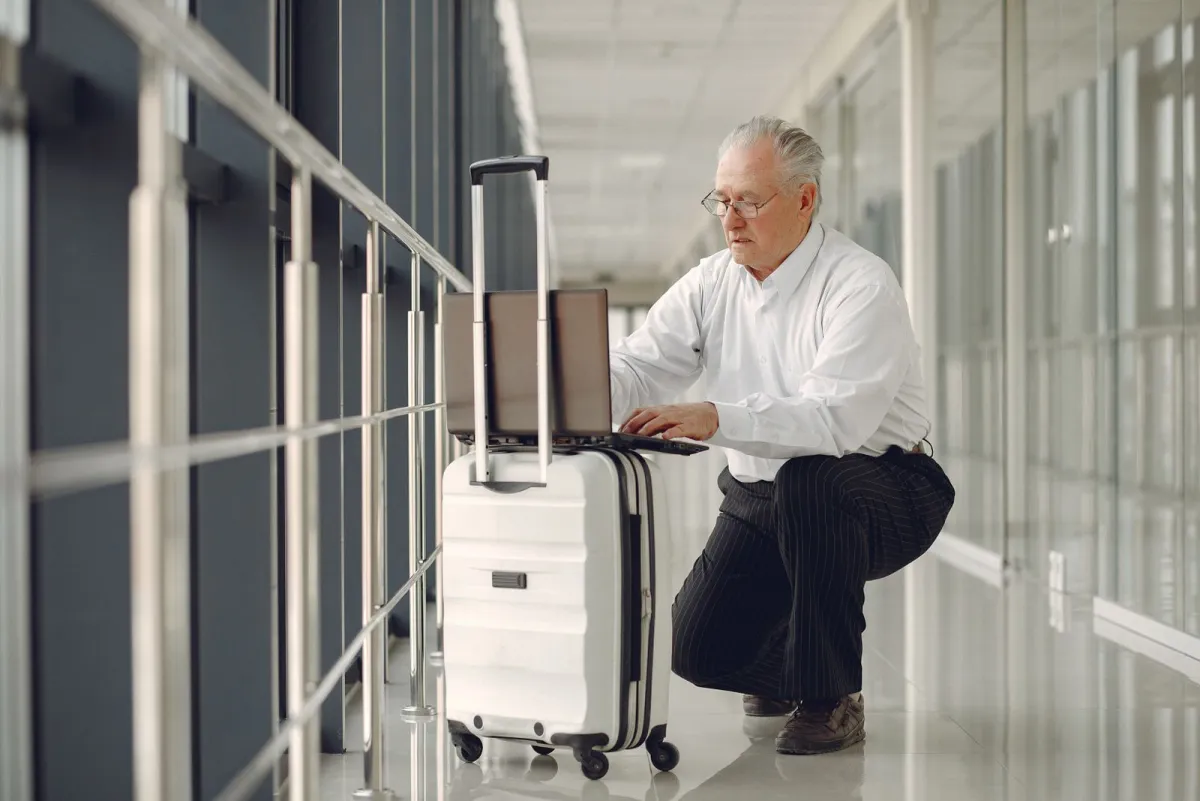 Traveler crouching in an airport corridor to use a laptop propped on a rolling case