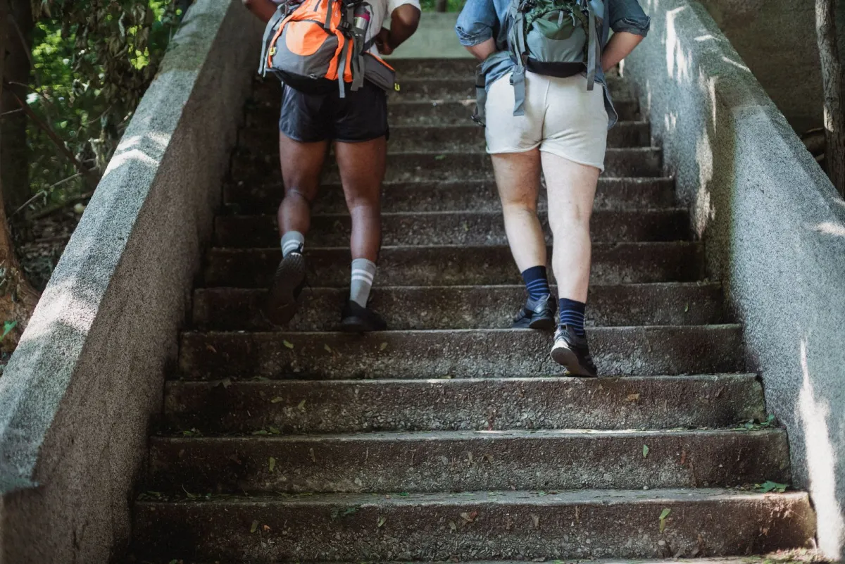 Two travelers with loaded backpacks climbing a long flight of worn stone steps