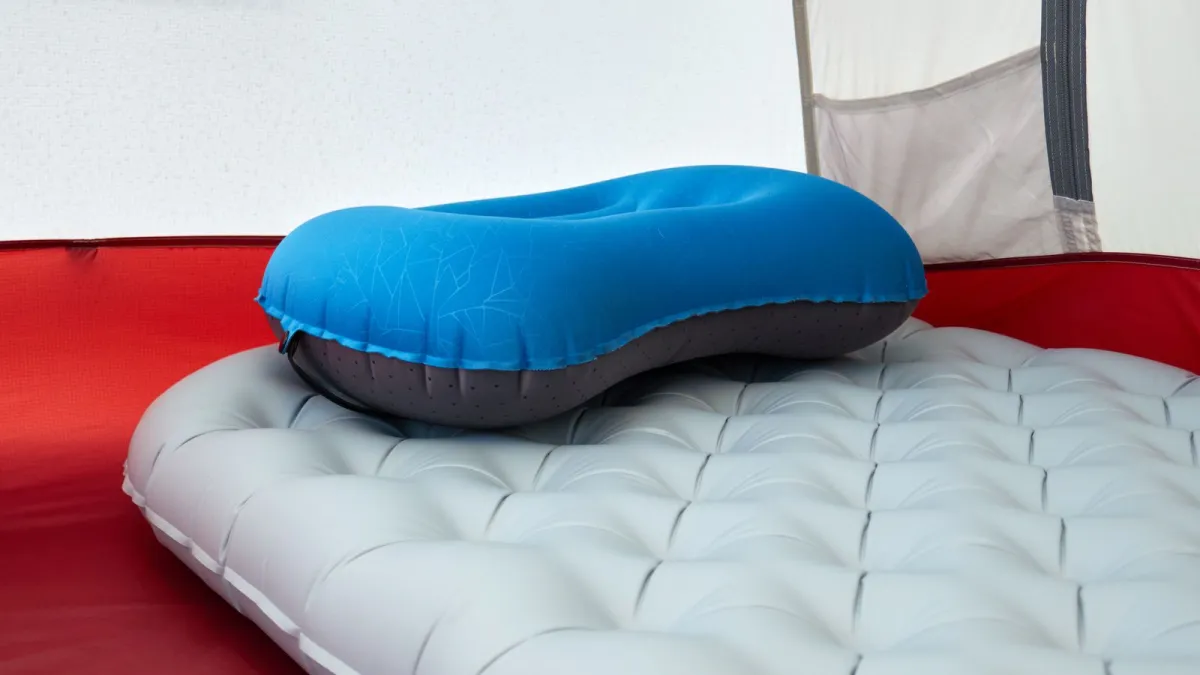Blue inflatable travel pillow set on an inflated sleeping pad inside a tent