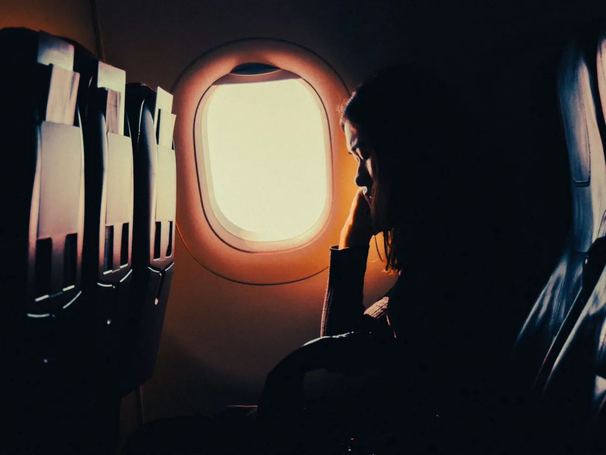 Passenger resting against a lit airplane window in a darkened cabin during a long flight