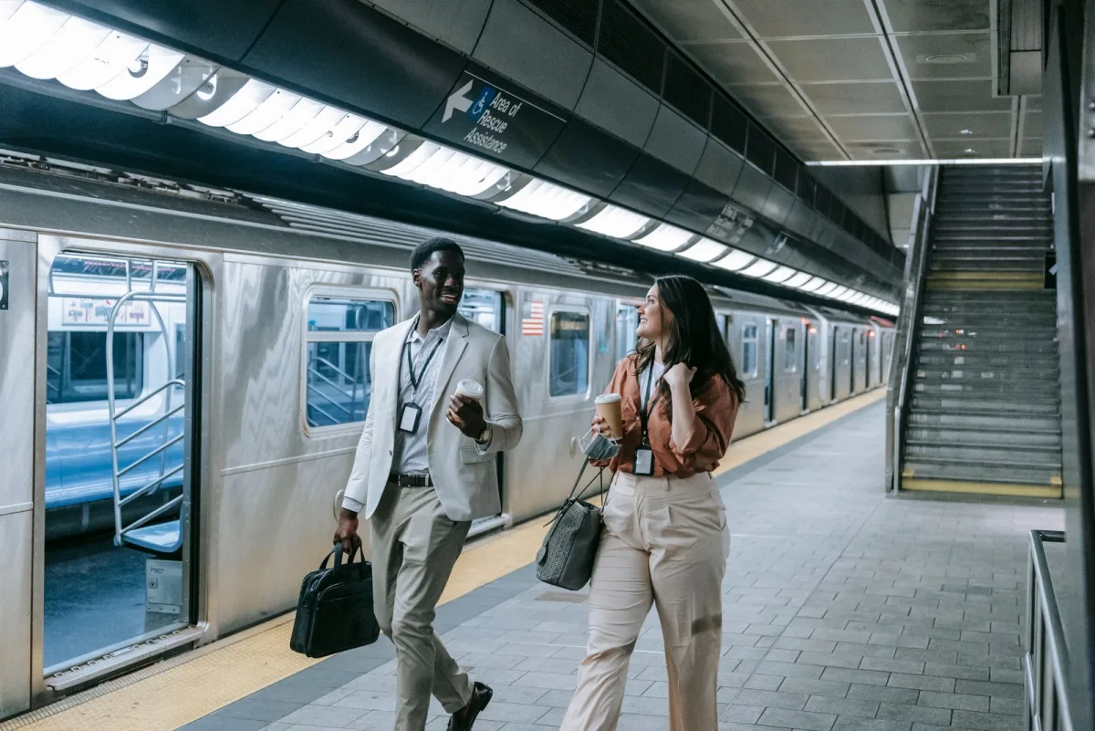 Two commuters with coffee and bags at a subway station