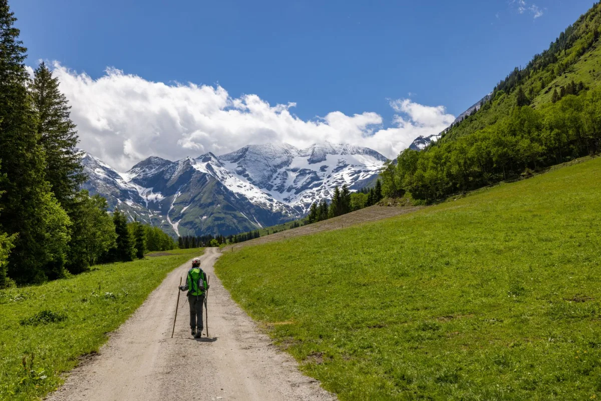 Walking a dirt road below snow-capped mountains with a pack