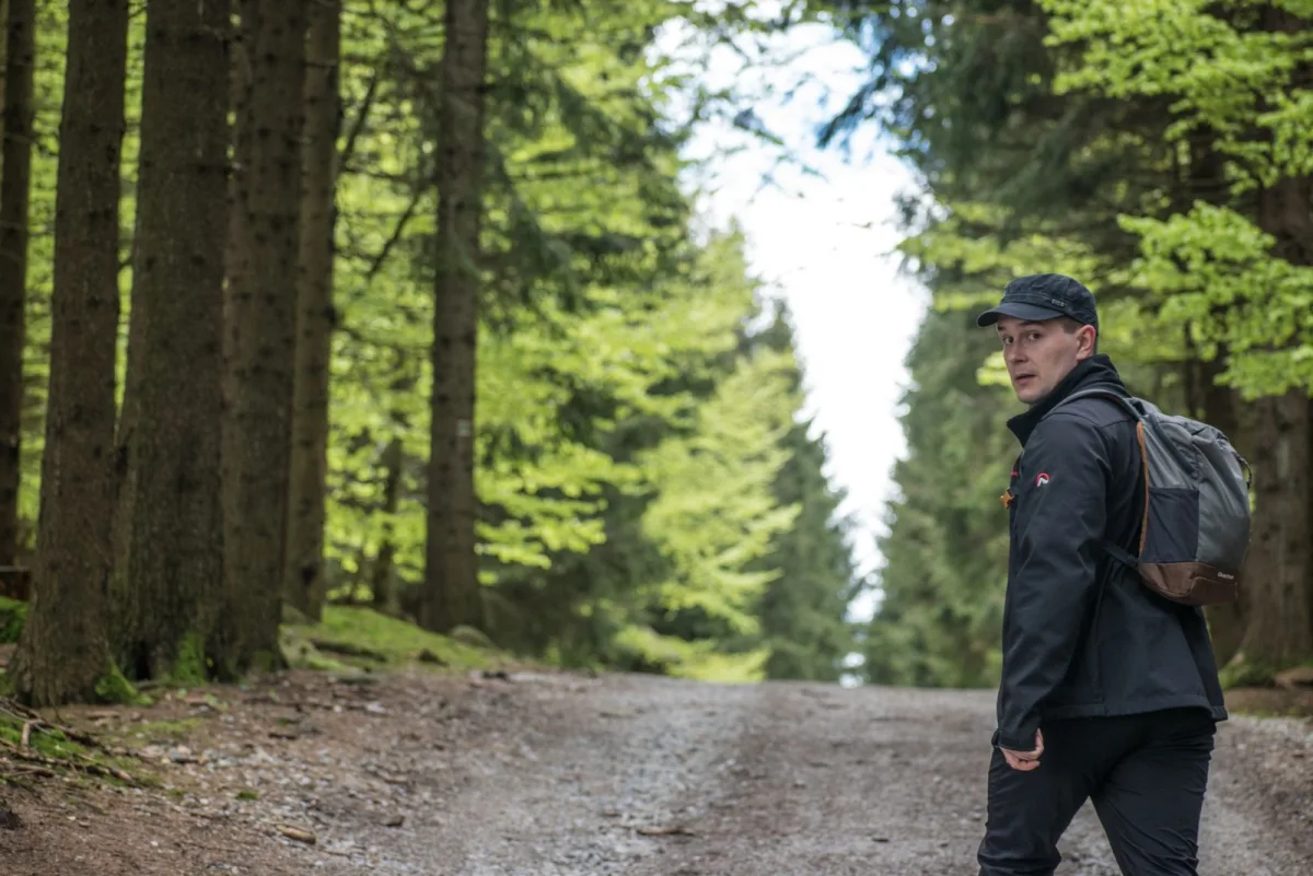 Walker on a green forest path carrying a pack