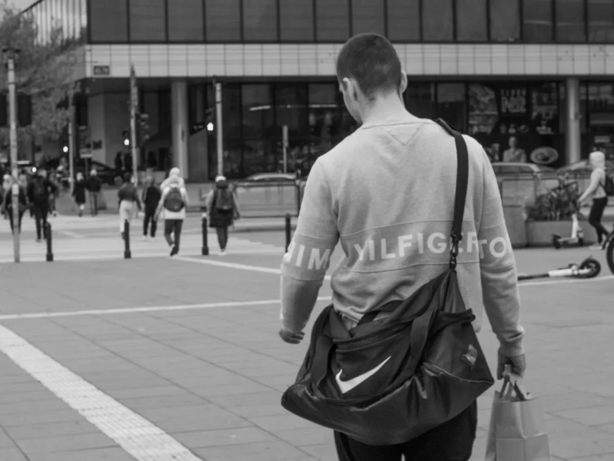 Black and white shot of a commuter crossing a city street with a shoulder bag across his back