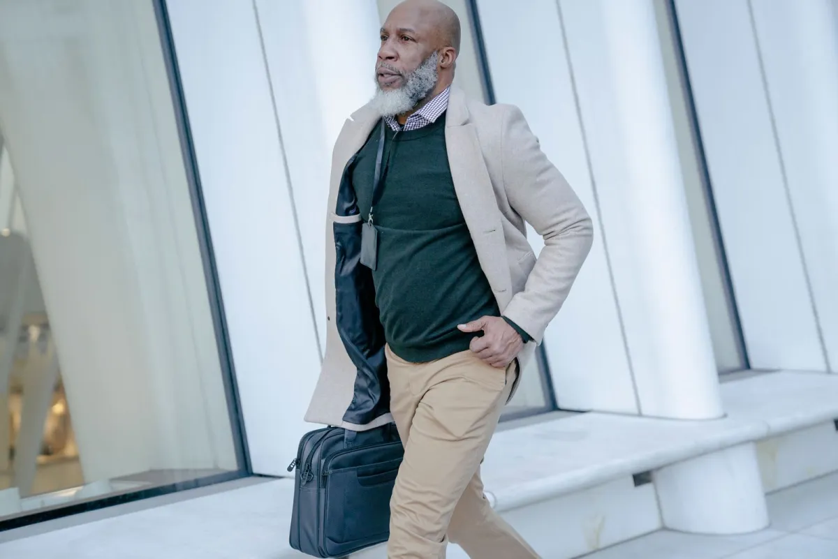 Man in a blazer carrying a slim laptop bag past the glass frontage of an office building