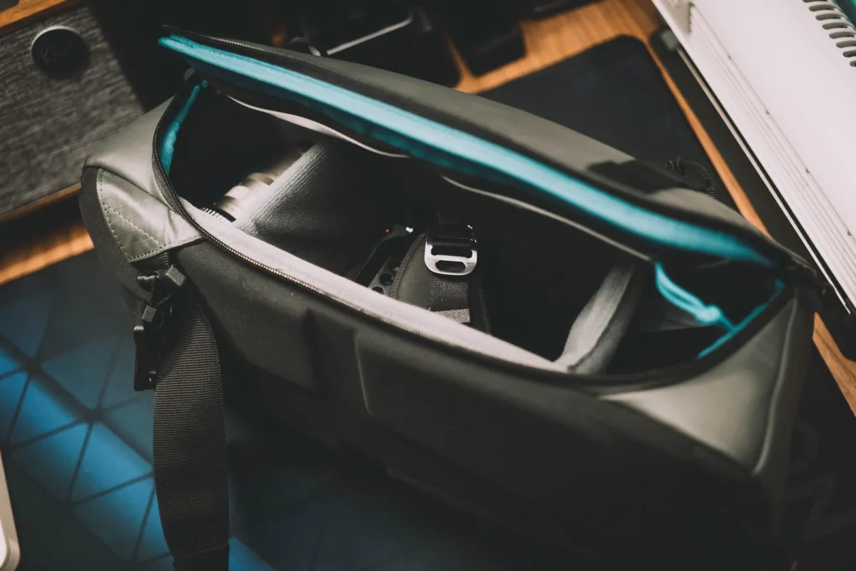 Open camera messenger bag on a desk with padded dividers around a lens and camera body
