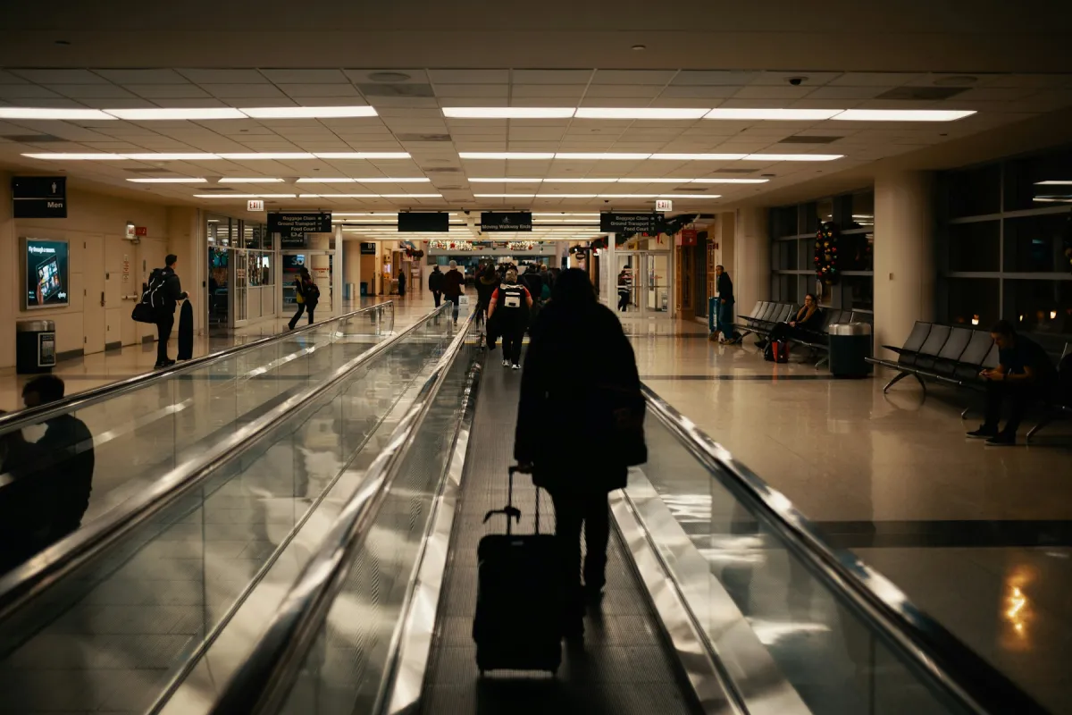 Traveler wheeling a hardside carry-on suitcase along an airport moving walkway