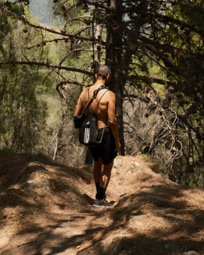 Robert Lora walking a pine forest trail with a black sling bag on his shoulder