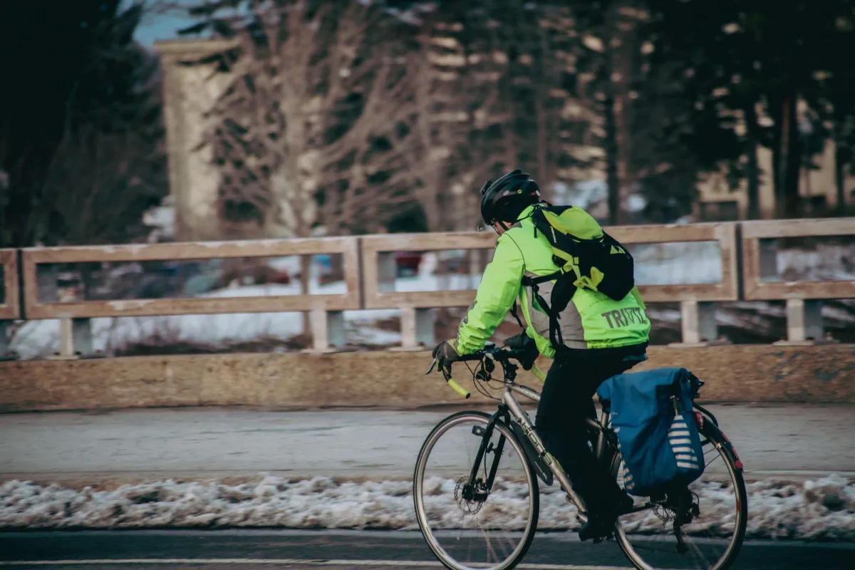 Cyclist in a high-visibility jacket riding a wet winter road with a blue waterproof pannier on the rear rack