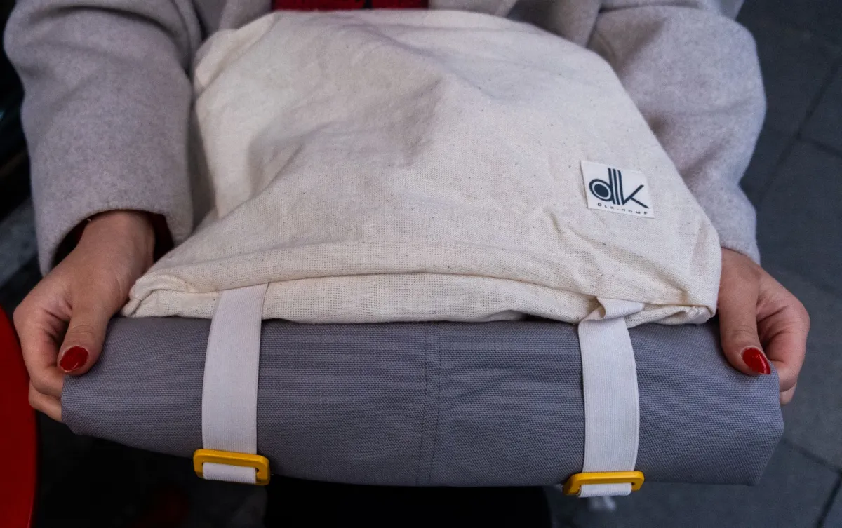 Hands holding a backpack with its top rolled down and secured by two webbing straps with yellow clips