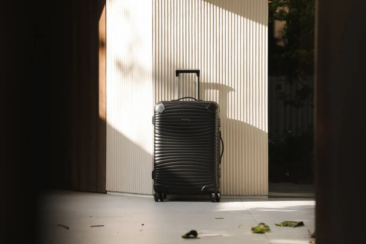 Black hardside spinner suitcase standing in a sunlit doorway