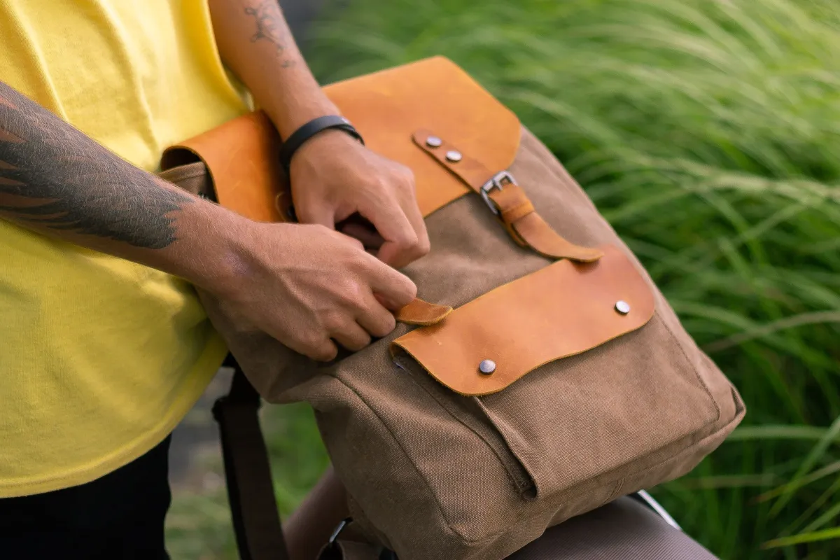 Hands fastening the leather strap on the flap of a canvas rucksack