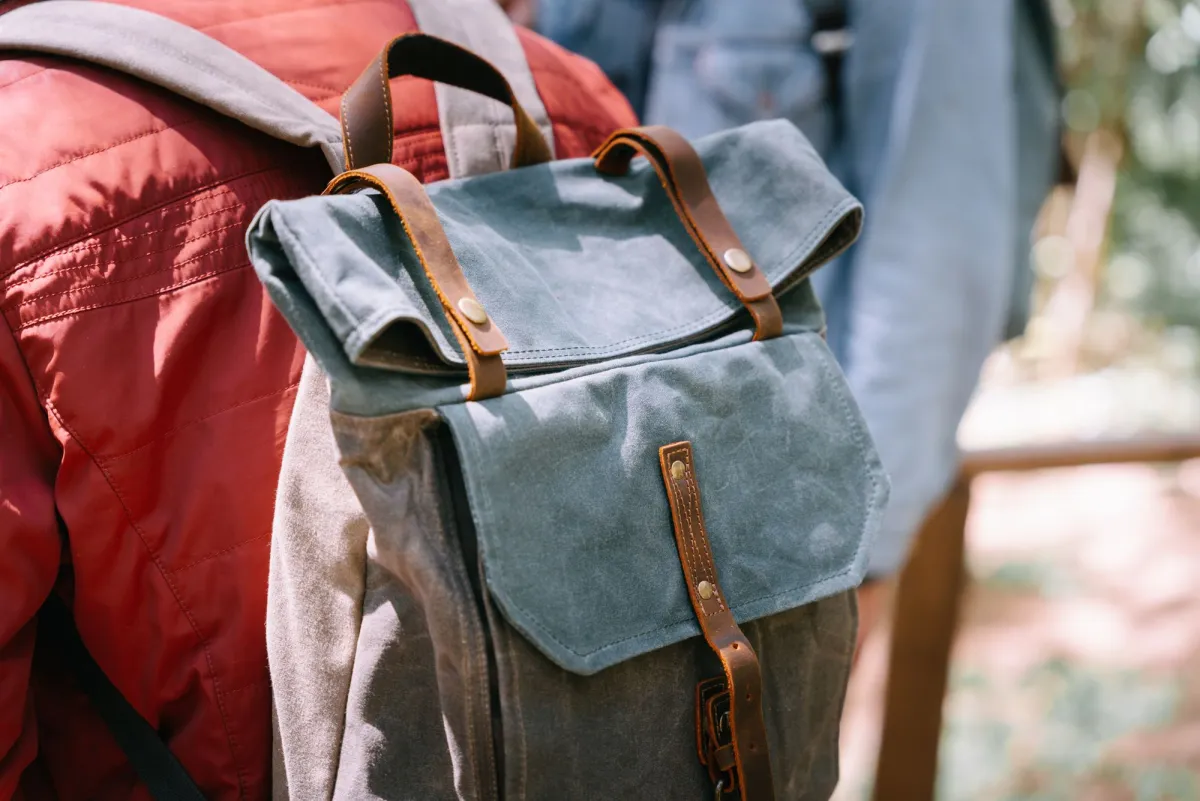 Waxed canvas rucksack with a buckled leather flap lid worn on a person's back outdoors