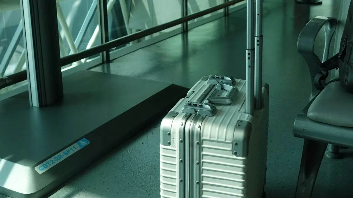 An aluminum carry-on suitcase standing beside empty seats at an airport departure gate