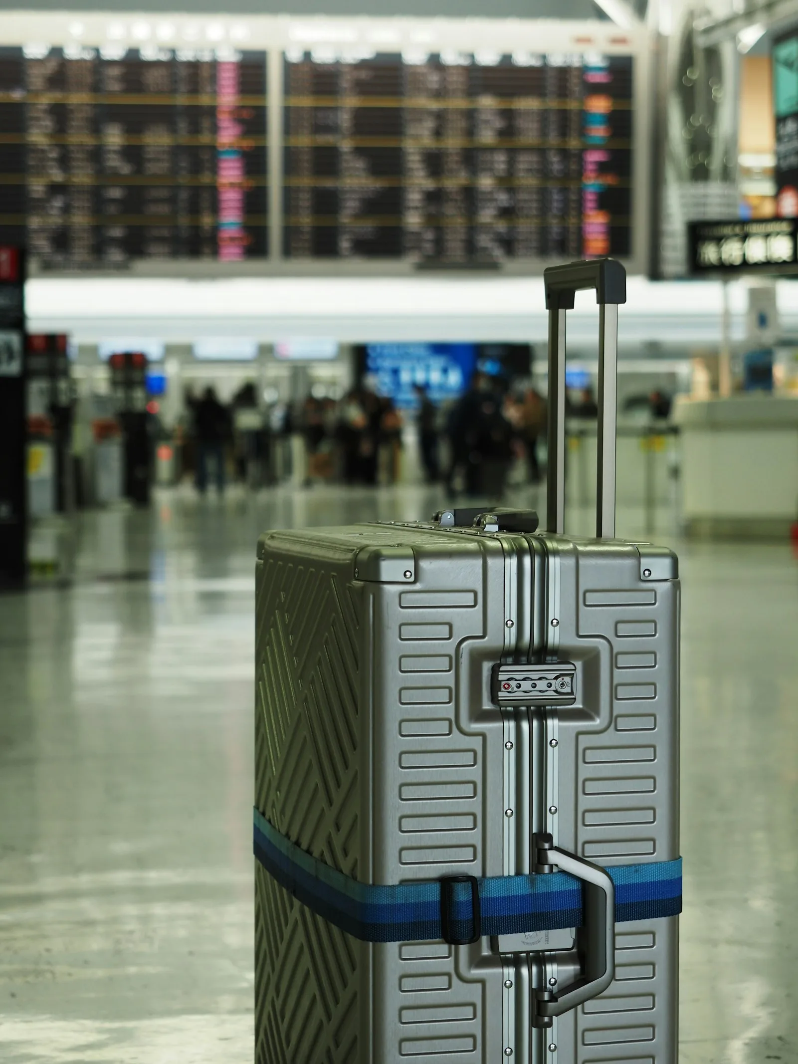 Silver grooved aluminum carry-on with its handle up in a bright airport terminal