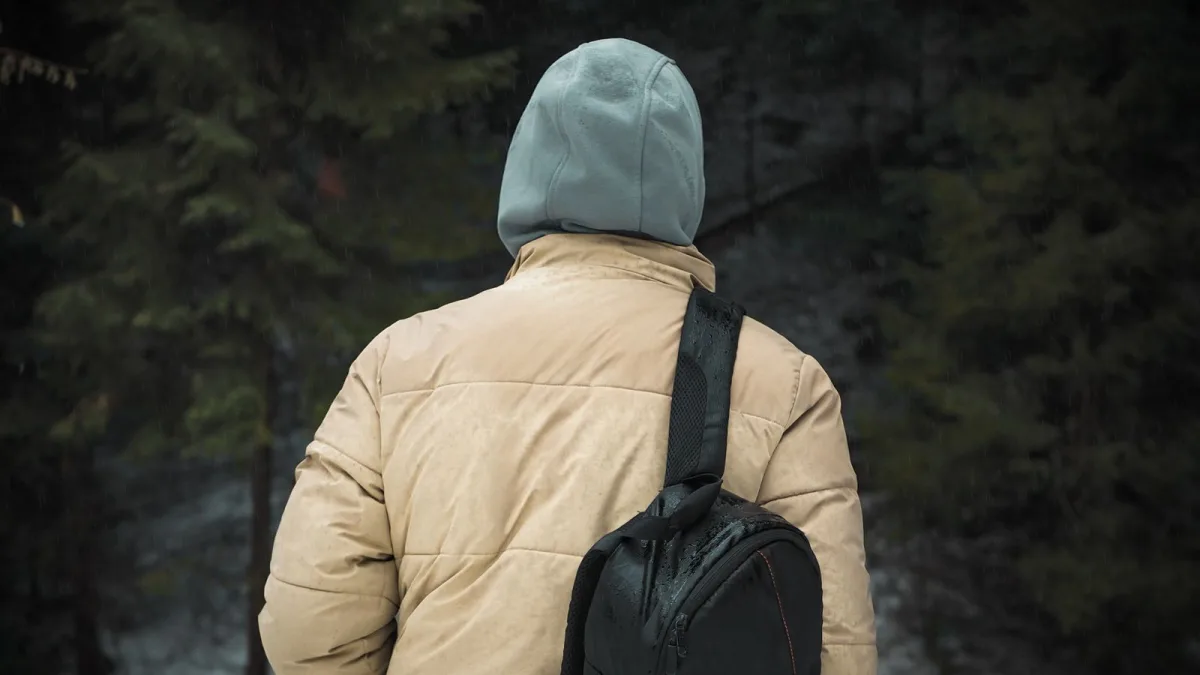 Hiker in a hooded jacket with a backpack in wet forest