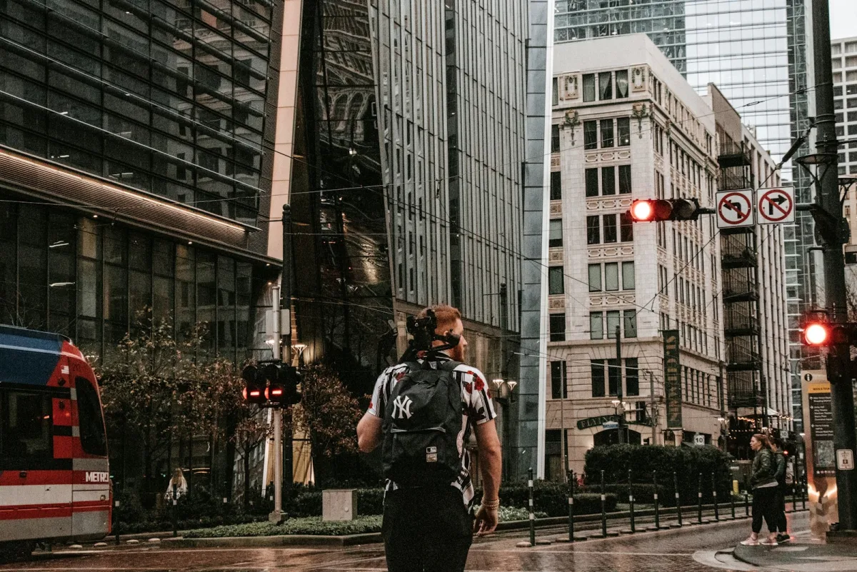 Man in a dark jacket waiting on a city sidewalk with a bag