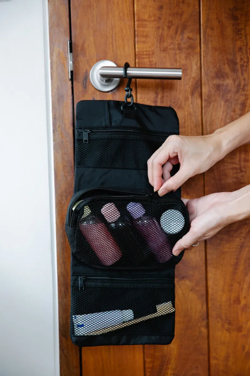 Hanging toiletry bag with travel bottles zipped into mesh pockets on a hotel door